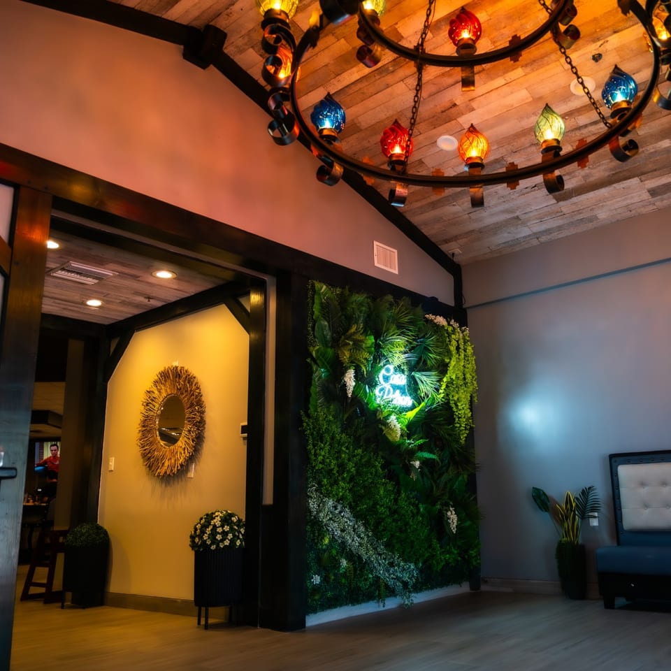 Casa Patron's entrance features a vibrant green wall with a neon sign, under a colorful chandelier.
