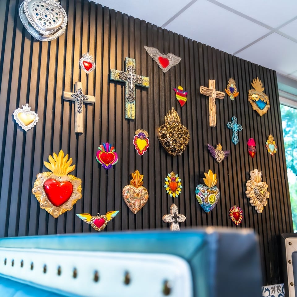 A dark slatted wall adorned with various colorful Mexican sacred heart and cross decorations.